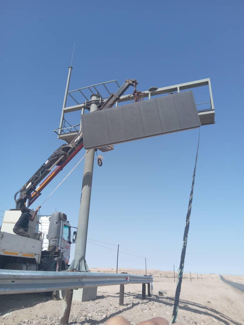 Crane hoisting a large LED display panel onto a roadside sign structure
