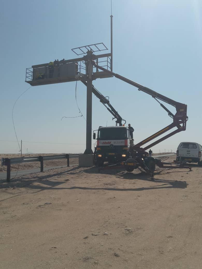 Crane truck lifting technicians into position to install a solar roadside sign