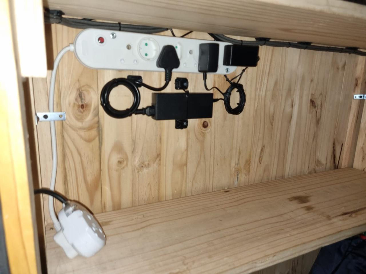 Power strip, adapters and cabling neatly secured inside a wooden cabinet