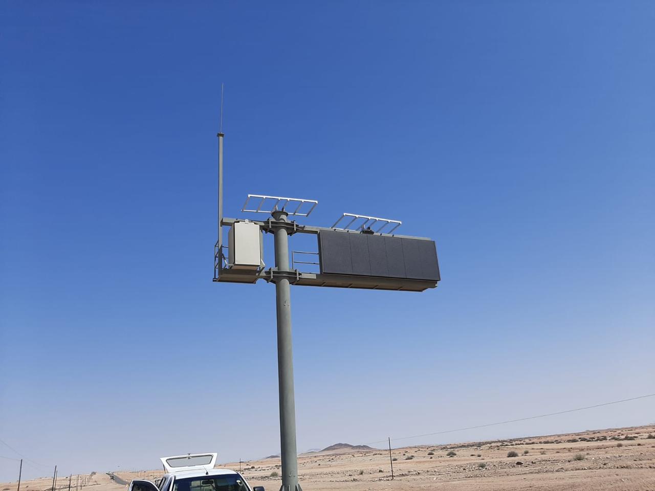 Solar-powered roadside sign installed on a tall steel pole in a desert region